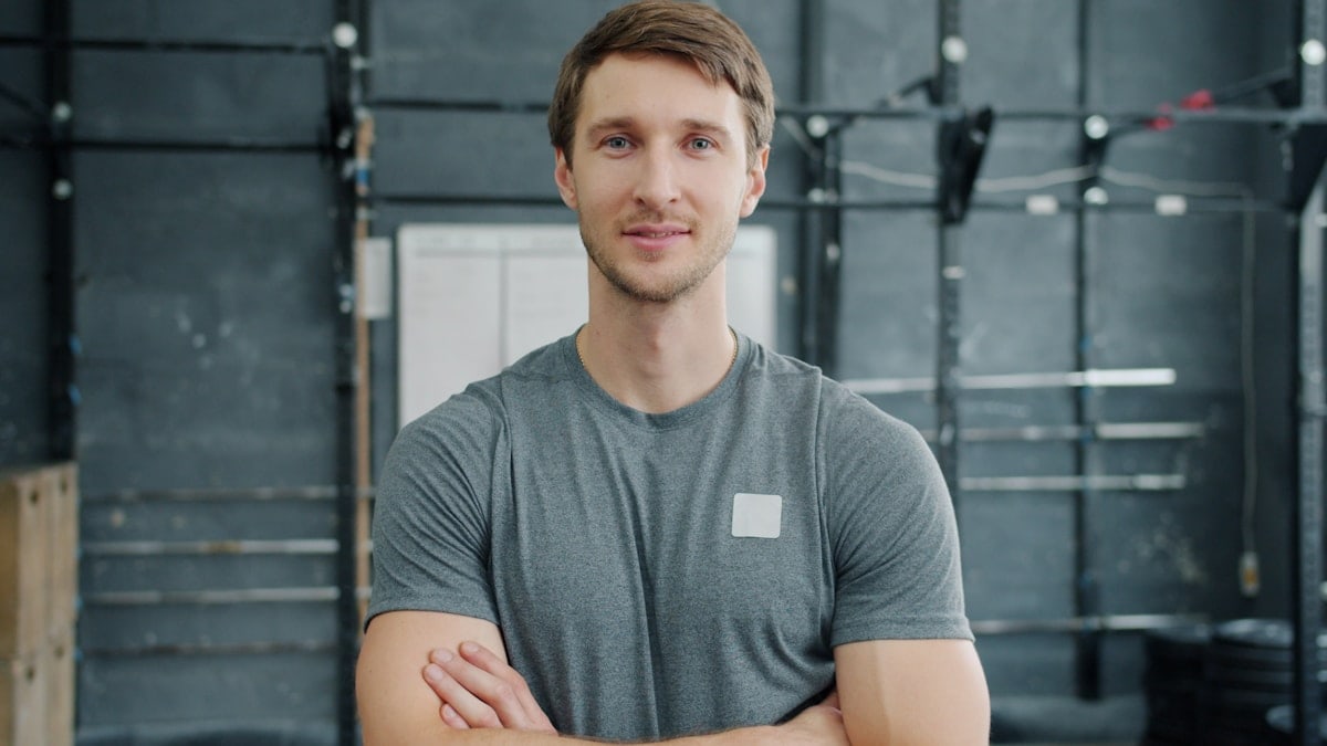 Portrait of young sportsman in sportswear standing in gym with arms crossed and looking at camera feeling confident and ambitious. People and sports concept.